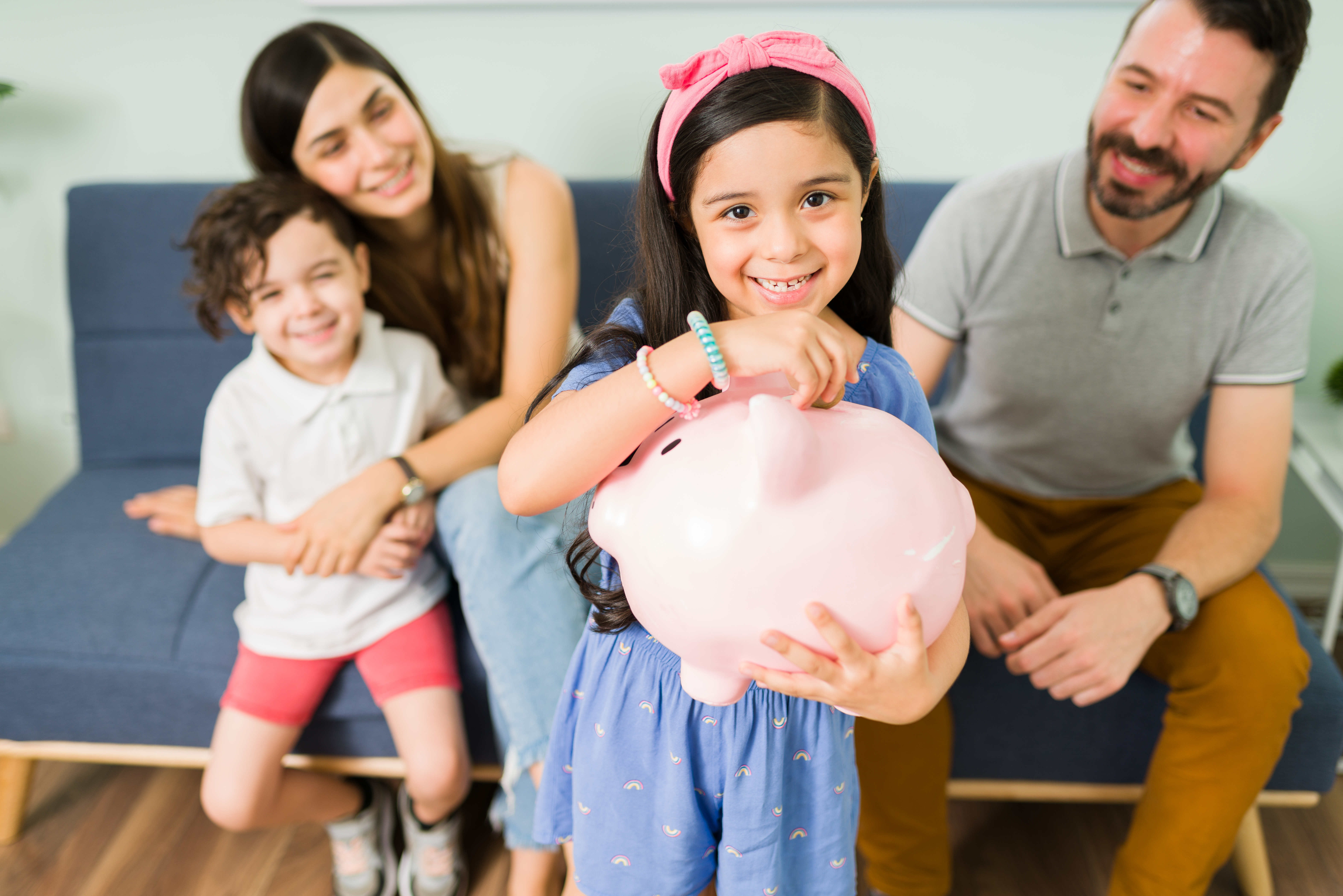 A girl holding her piggy bank while her family watching at the back smiling